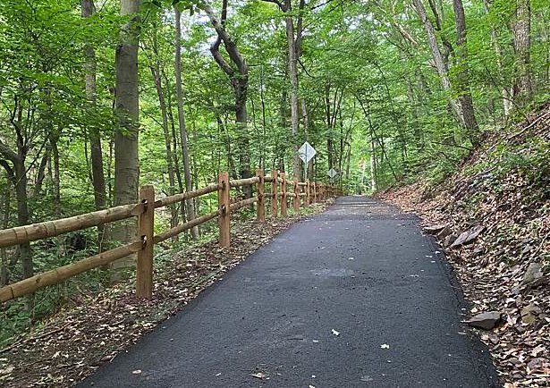 Wooded paved trail with a split-rail fence near Audubon