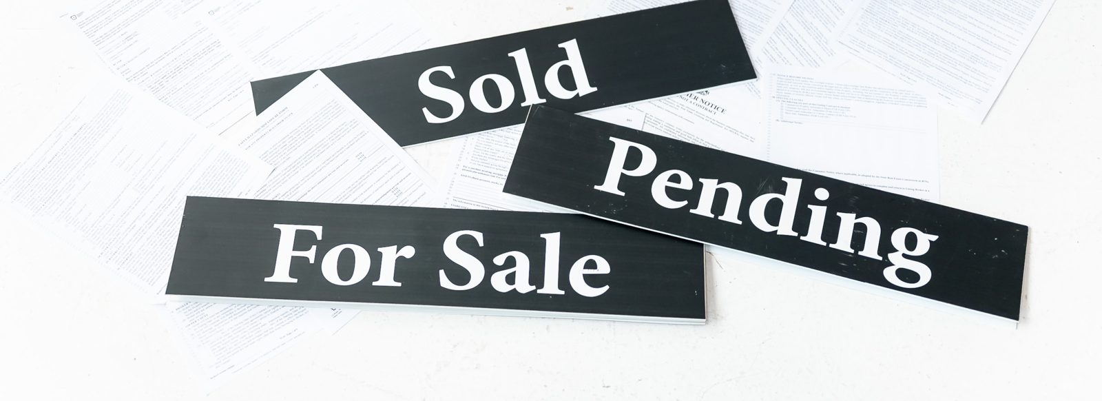 For Sale, Pending and Sold signs on a spread of real estate paperwork